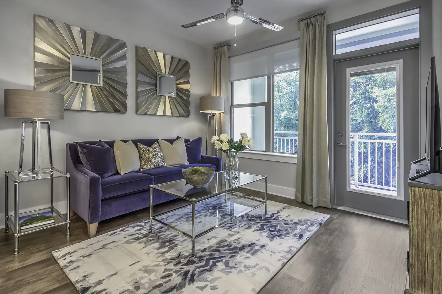 Living room with purple couch, glass coffee table, and sunburst mirrors.