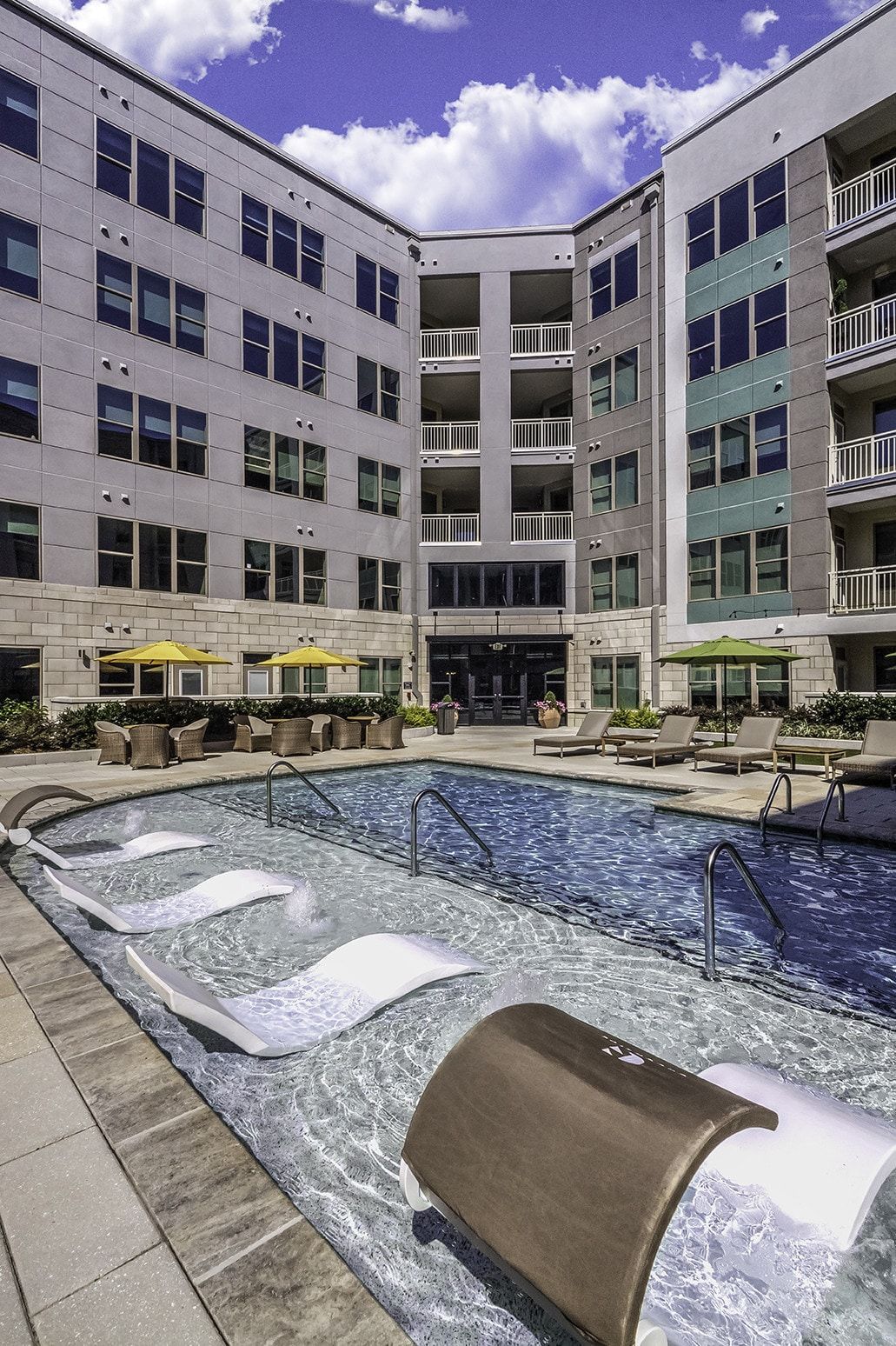 Swimming pool with lounge chairs at an apartment complex, surrounded by buildings with balconies.