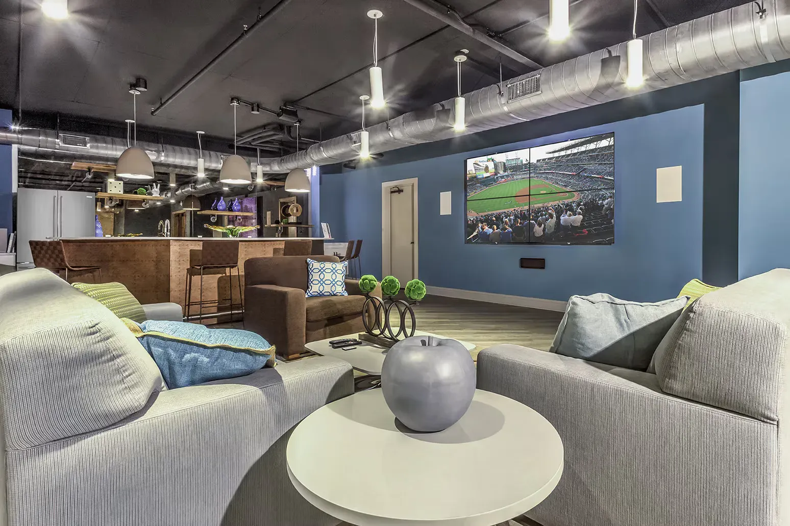 Spacious lounge with couches, a bar, and a large screen displaying a sports game.
