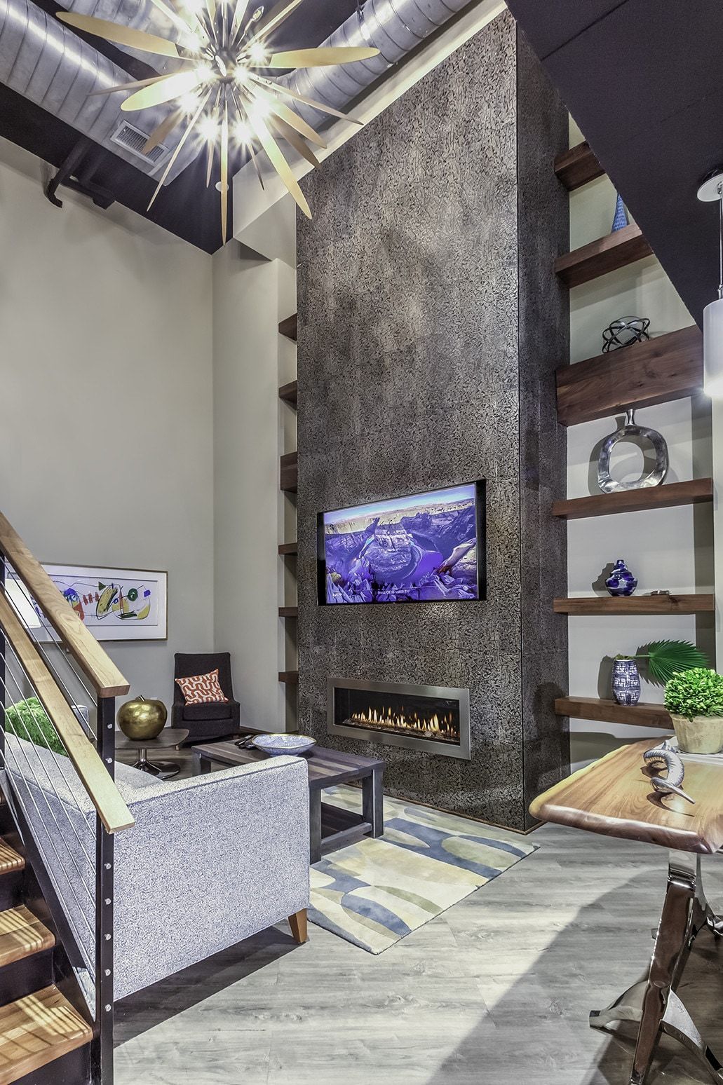 Living room with fireplace, TV, and built-in shelves. Gray and neutral color scheme. Stairs visible on left.