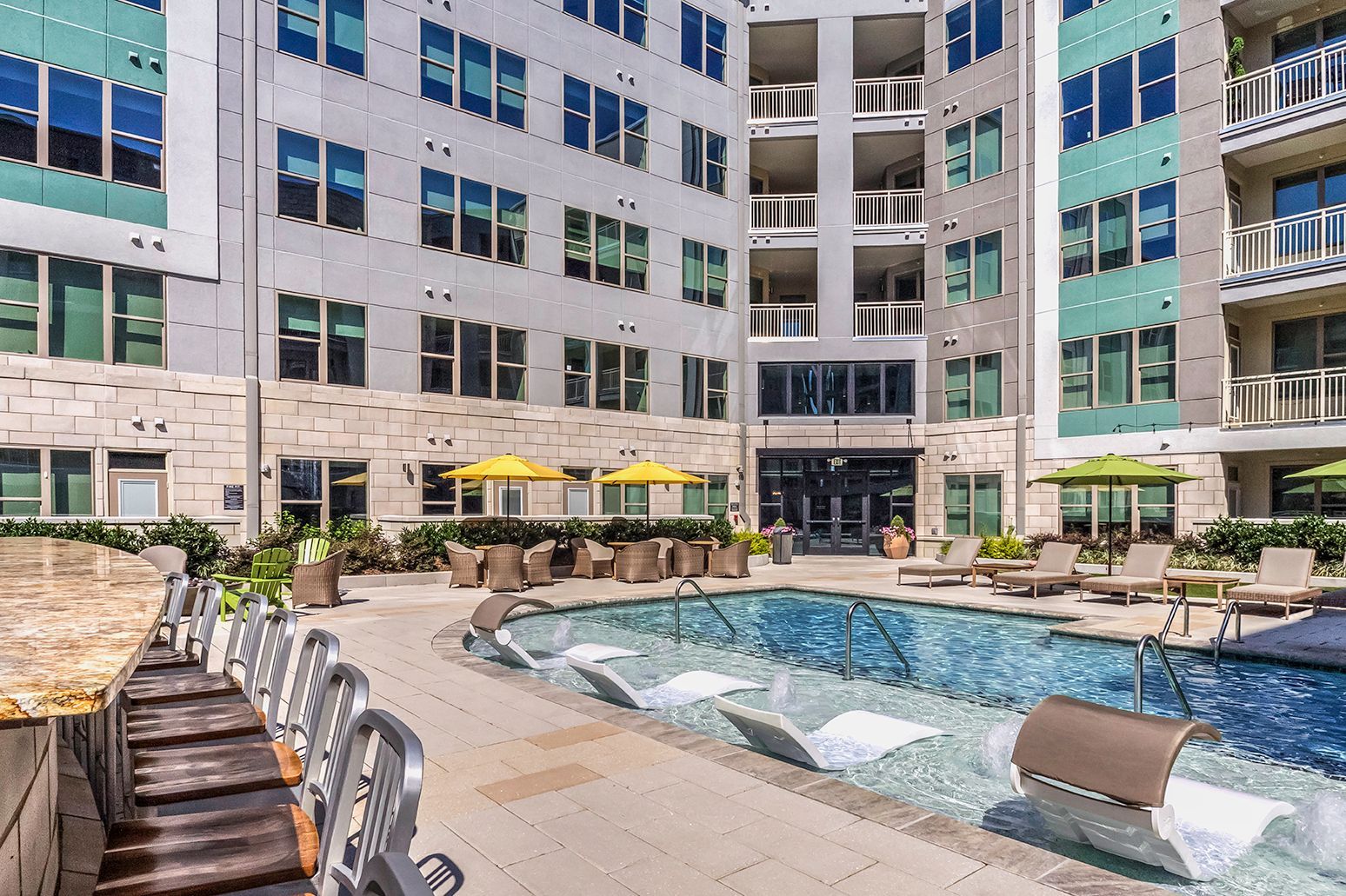 Outdoor pool area with lounge chairs, yellow umbrellas, and a modern apartment courtyard.