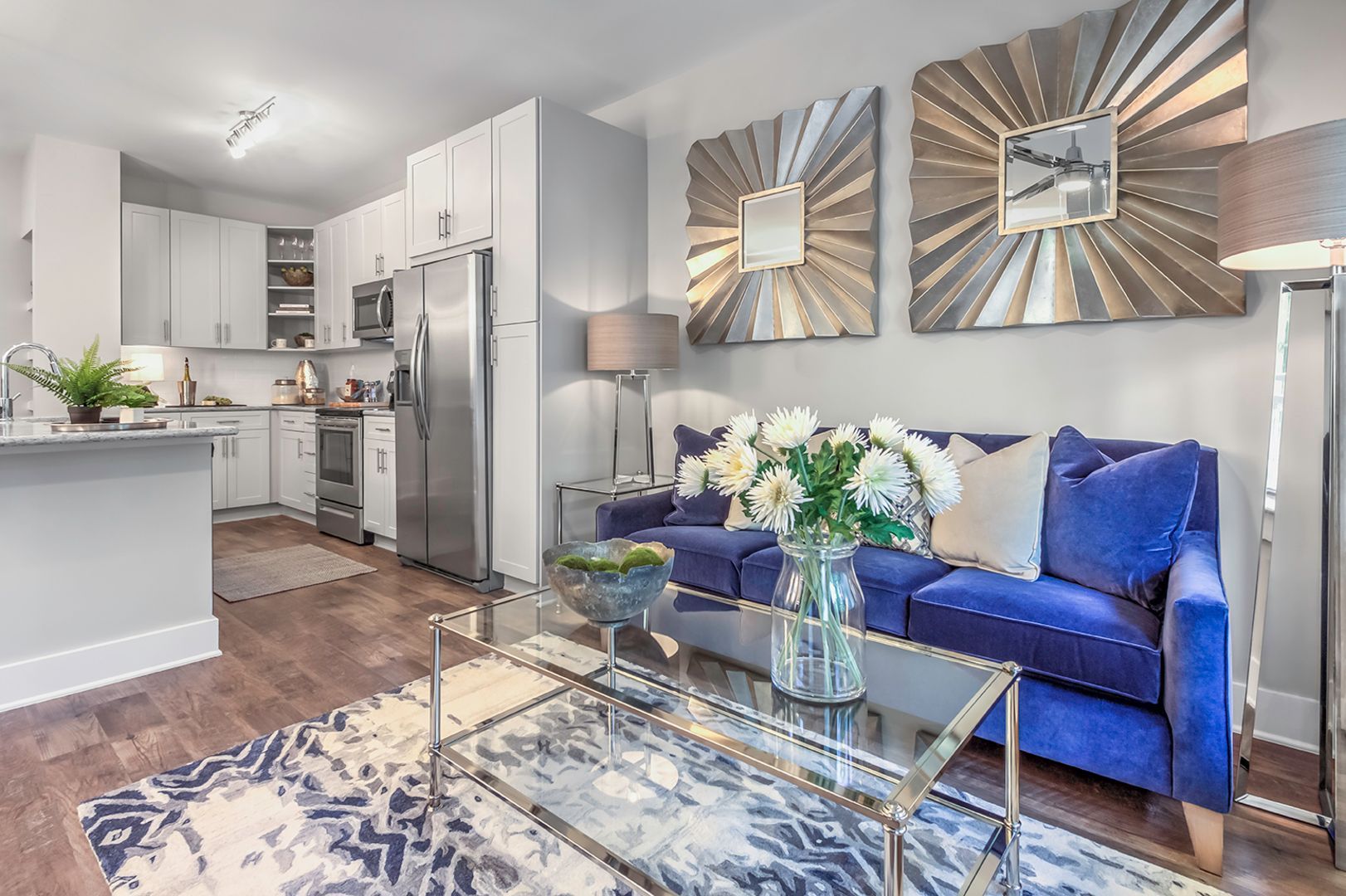 Open-concept living area with white kitchen cabinets, stainless steel appliances, and a blue sofa.