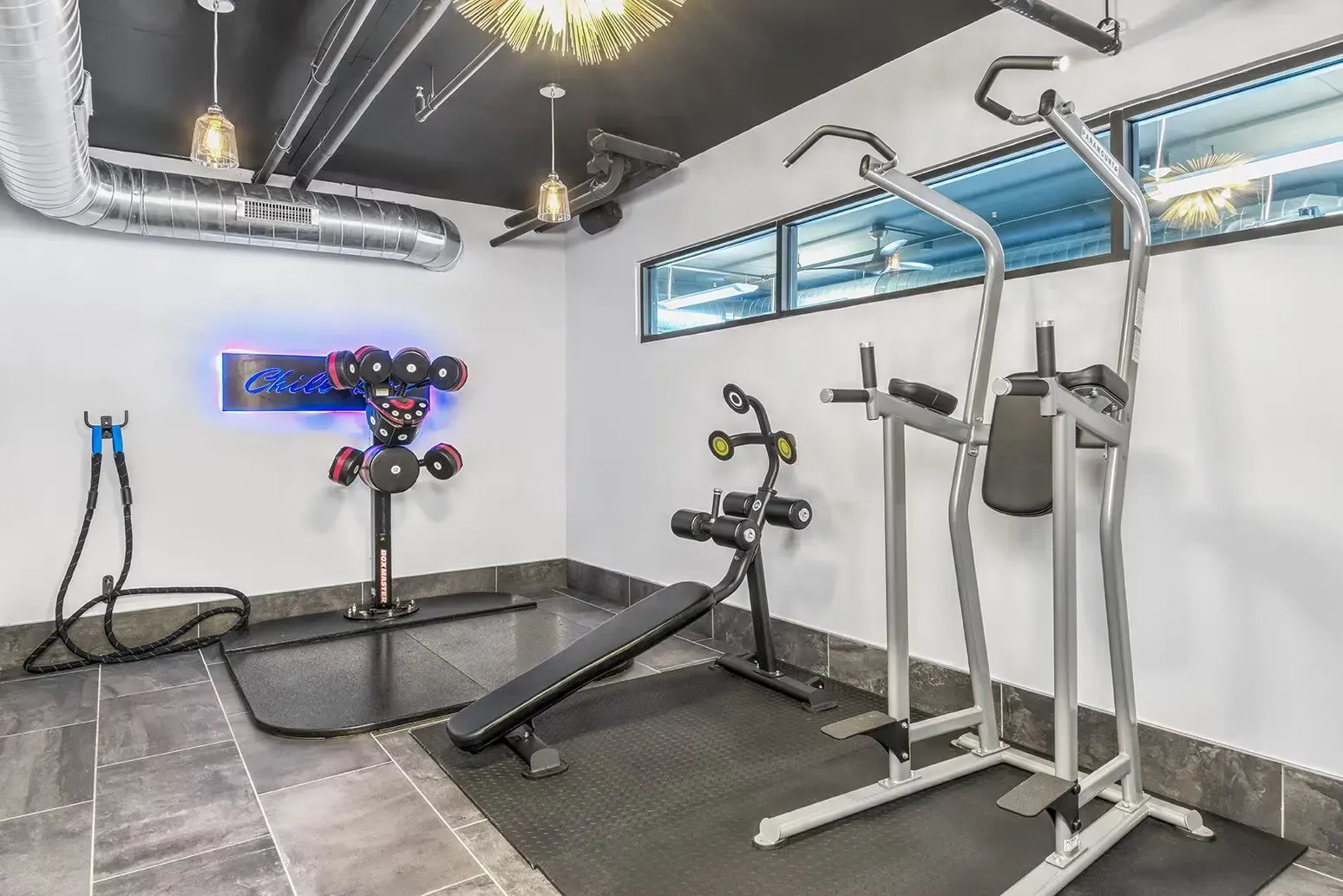 Home gym with various exercise equipment on a black mat, white walls, and a window.