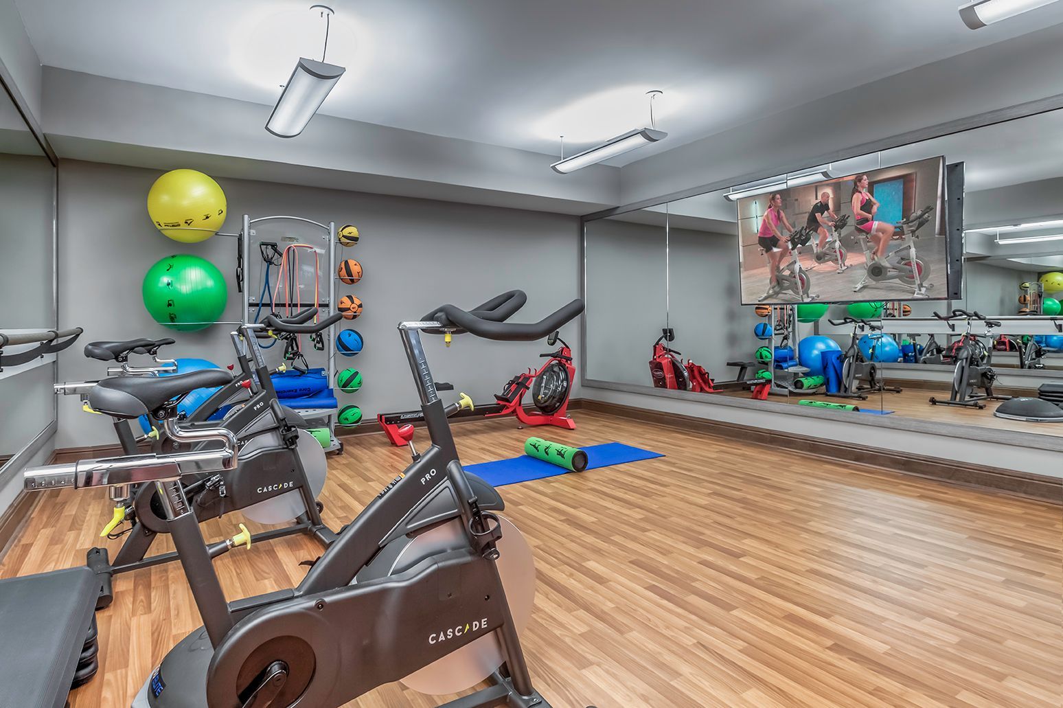Indoor community gym with stationary bikes, stability balls, and a mirrored wall.