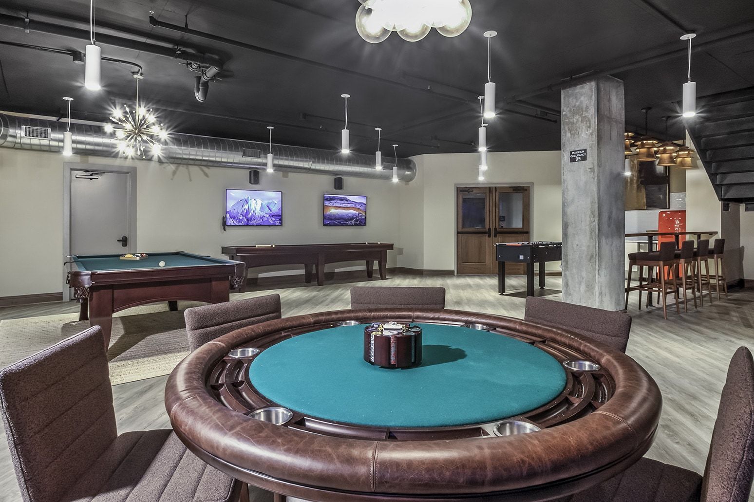 Game room with poker table, pool table, and bar. The room has dark ceilings and neutral walls.