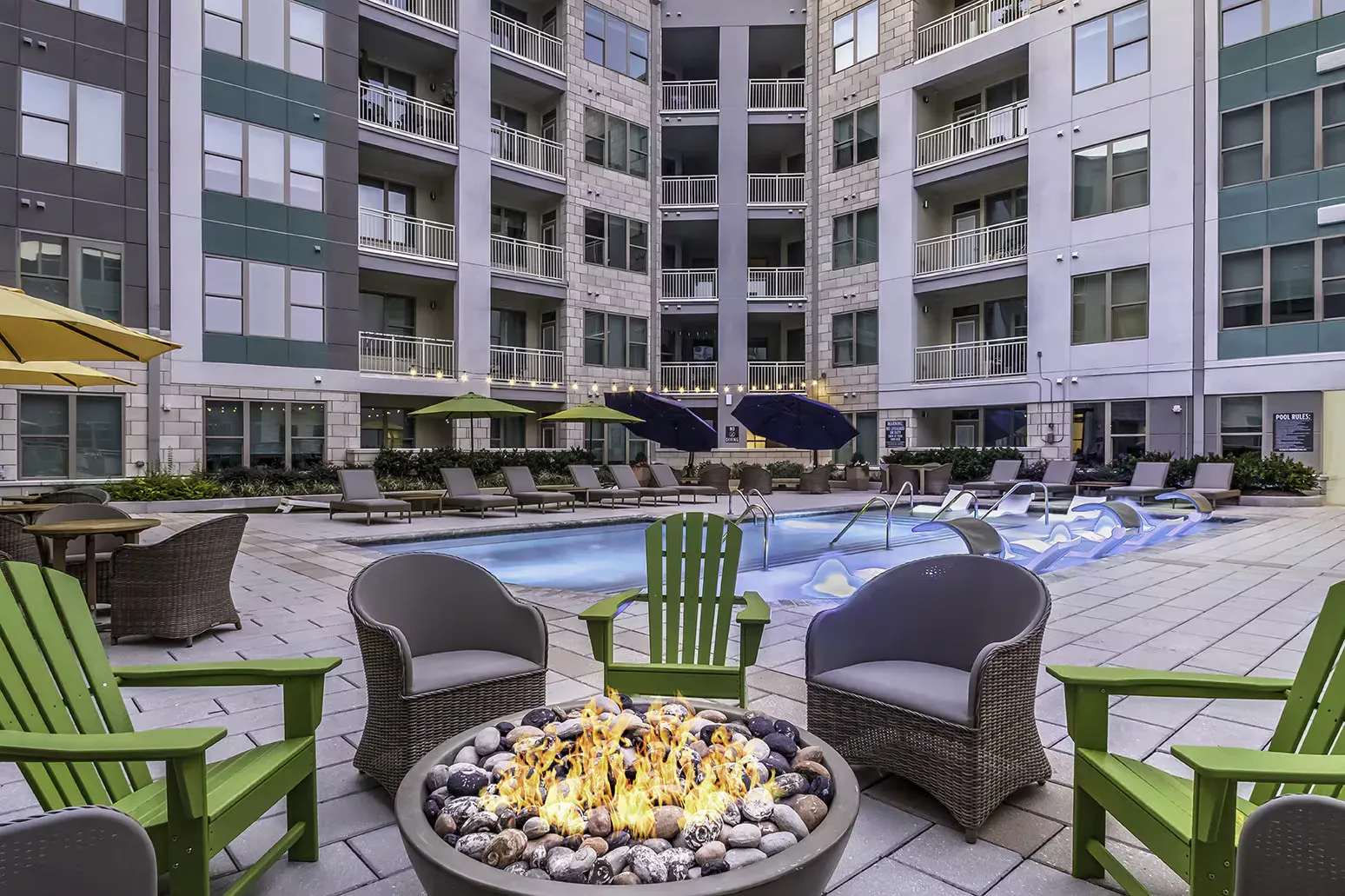 An outdoor courtyard with a pool, lounge chairs, and a fire pit in front of a multi-story apartment building.