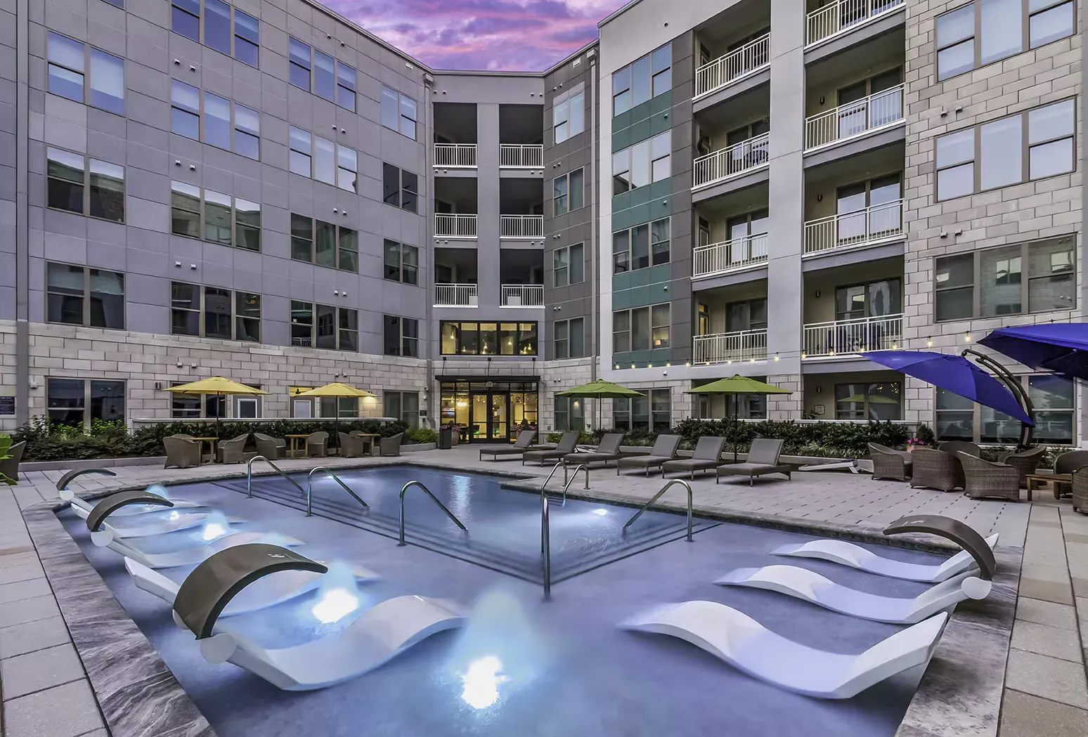 Pool area at an apartment complex, with lounge chairs in the water and buildings in the background.