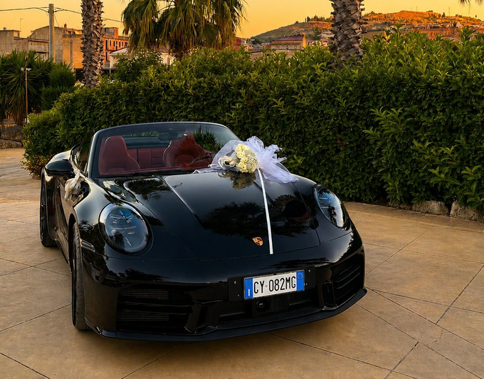Auto sportiva nera decorata con fiori bianchi, parcheggiata all'aperto al tramonto.