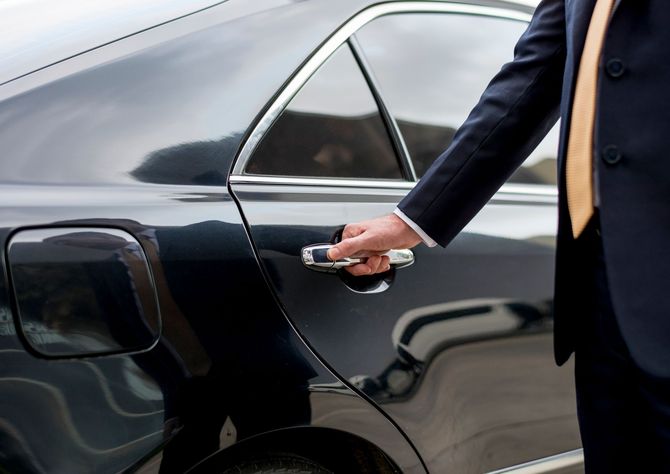 Una mano in abito scuro apre la portiera di un'auto nera