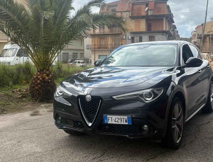 Interni di un'auto sportiva decappottabile rossa con sedili e cruscotto in pelle rossa, in viaggio su strada con la capote abbassata.