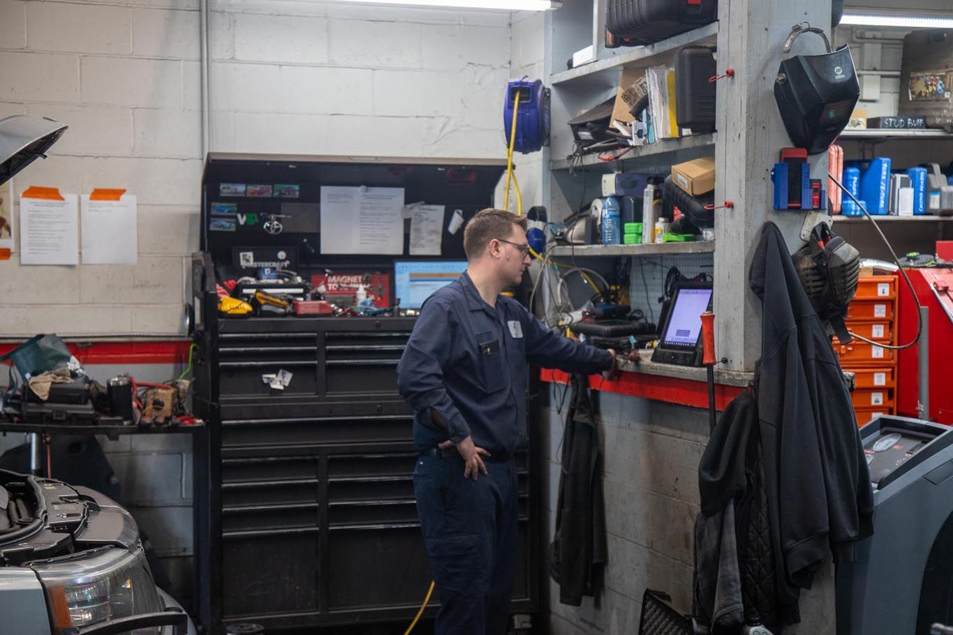 Mechanic working at a car repair station with tool chests, shelves, and hanging coats