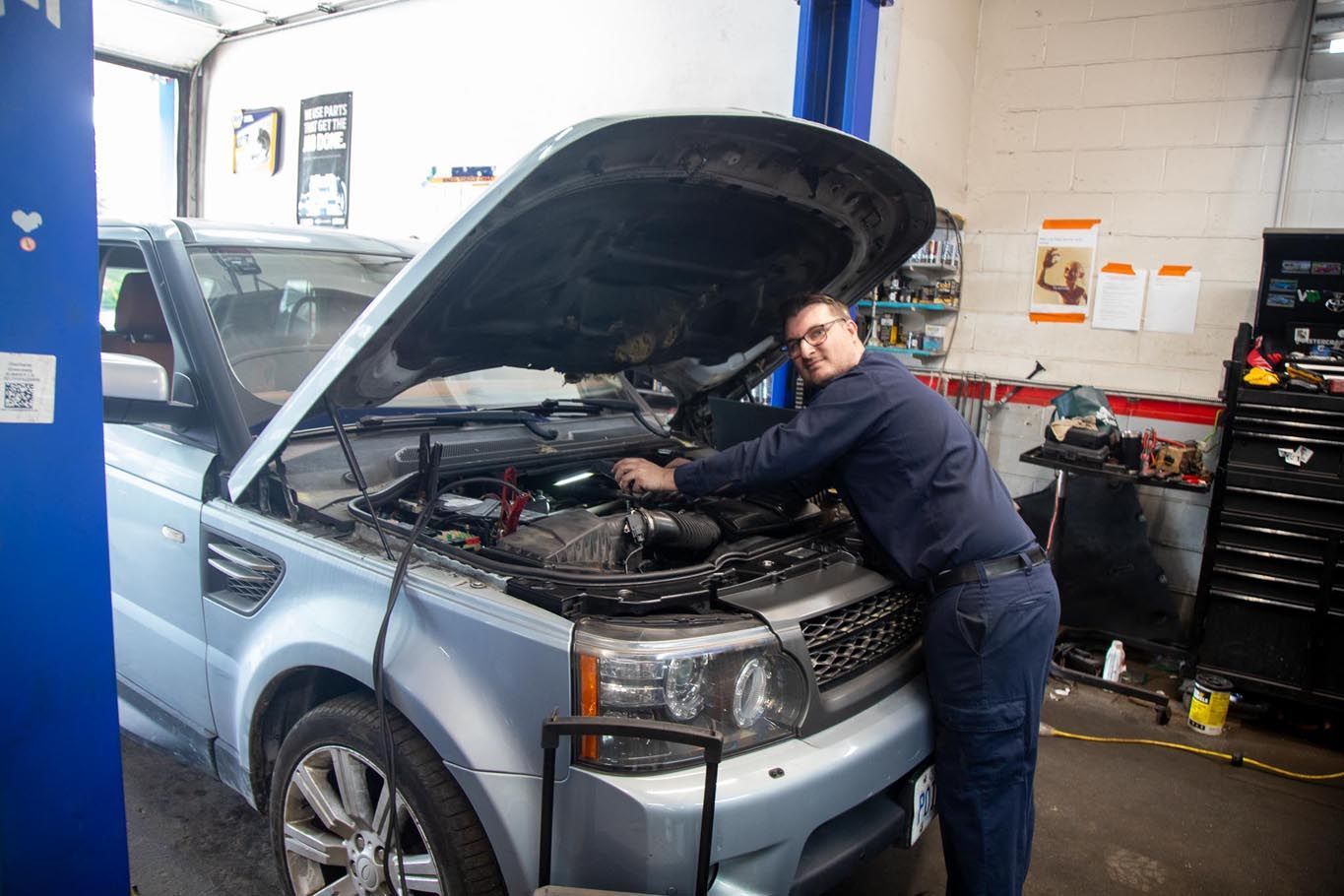 Mechanic working under the hood of a silver SUV in an auto repair shop
