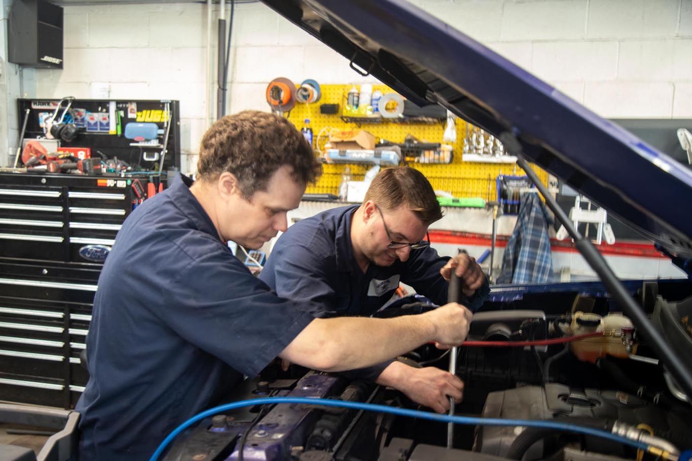 Two mechanics working under a car hood in an auto repair garage