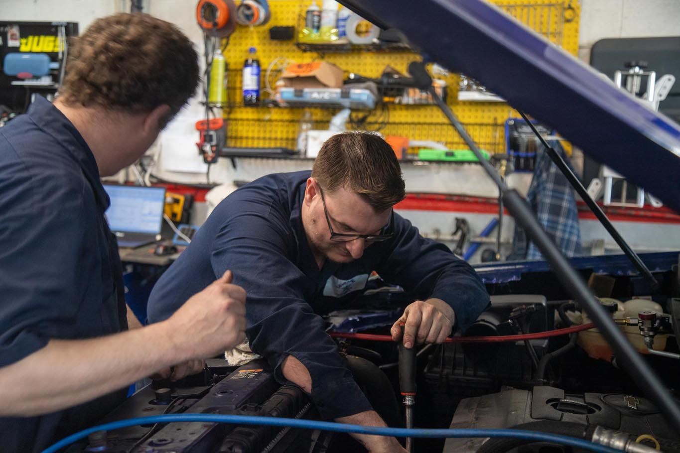 Two mechanics in a garage working on a car engine under the hood
