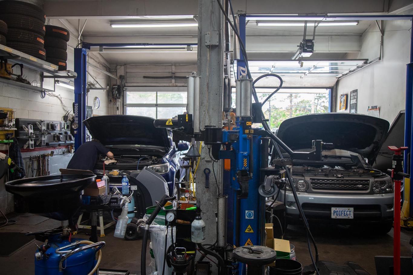 Auto repair shop with two cars on lifts, both hoods open, and tools scattered around the garage.