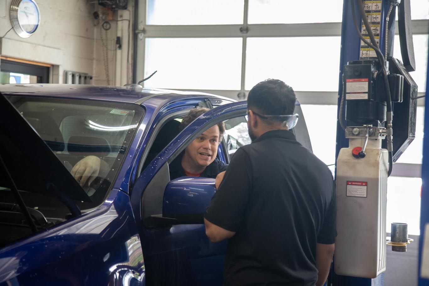 Man speaking with a driver at a blue SUV inside a garage service bay