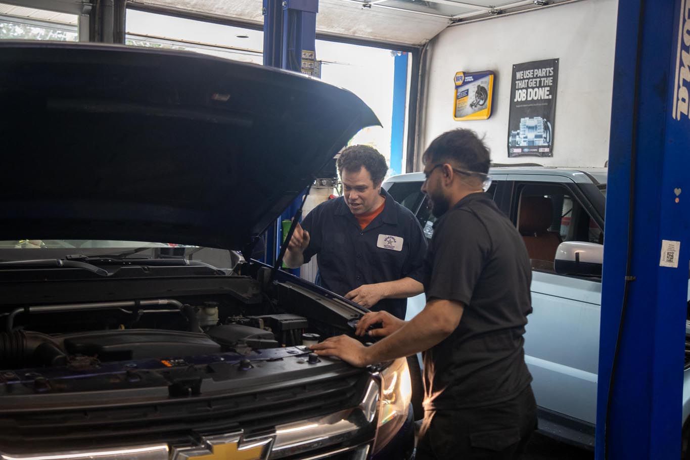 Two mechanics inspecting an open car hood in an auto repair shop