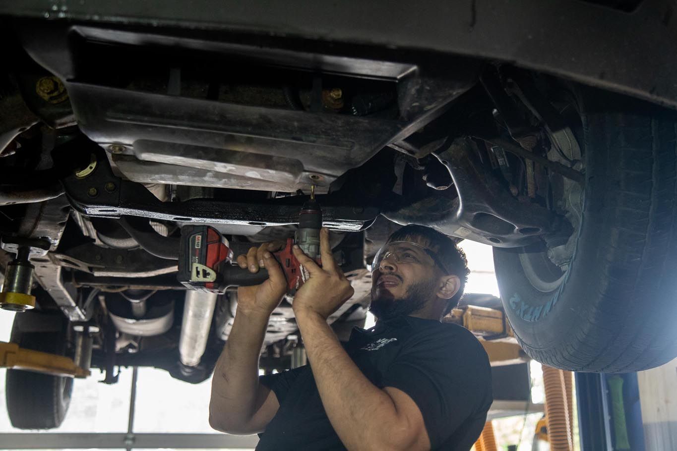 Mechanic working under a car, tightening parts with tools in a garage lift