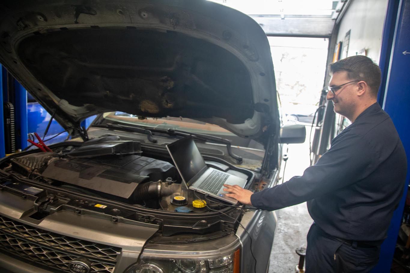 Mechanic inspecting an open car hood in a repair shop, using a diagnostic tool