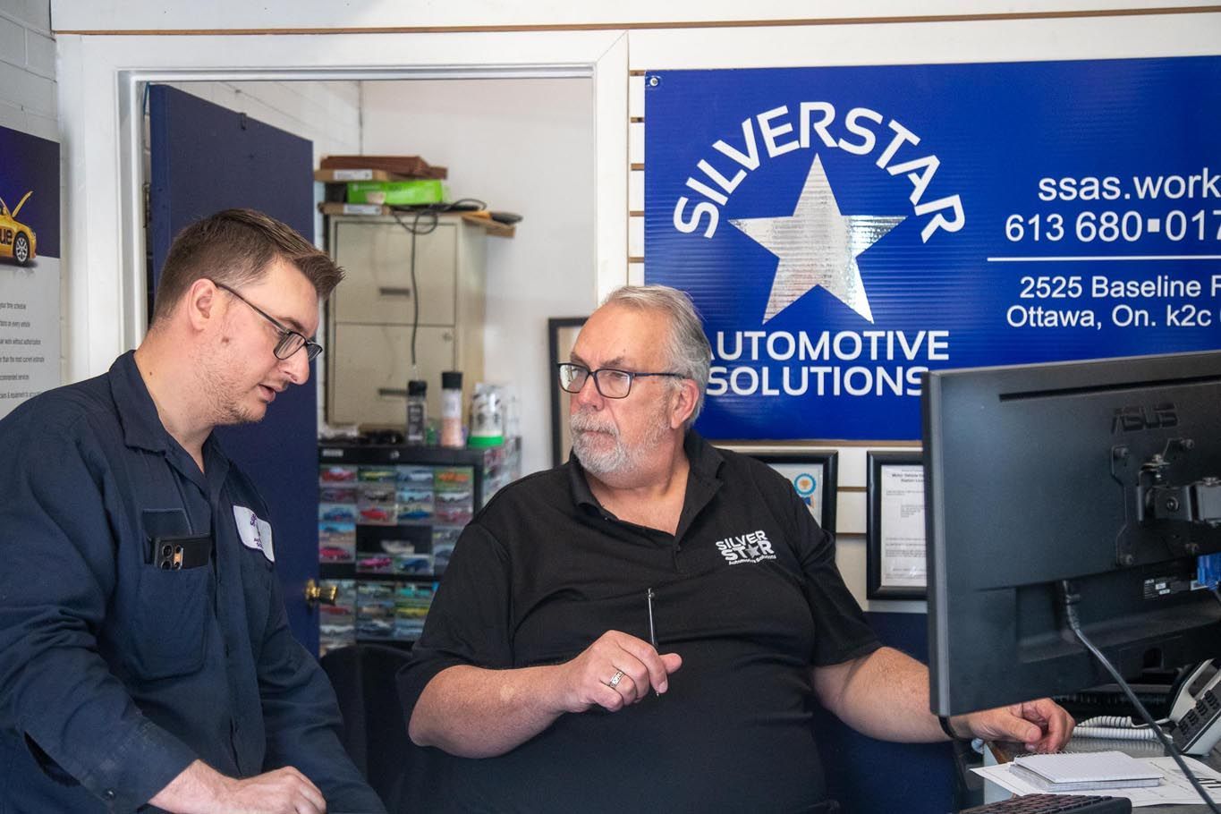 Two men talking in an office beside a computer and a “Silverstar Automotive Solutions” sign