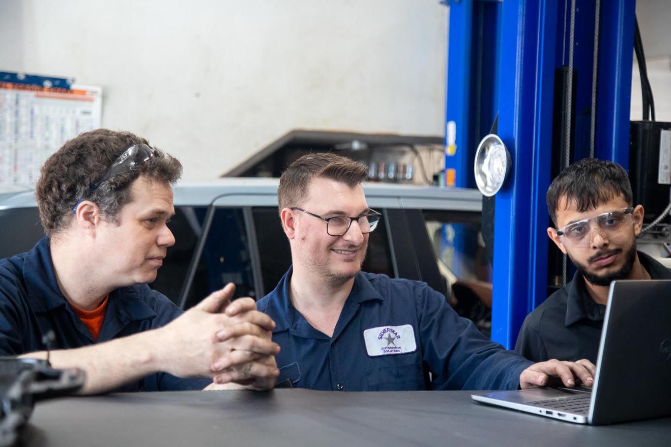 Three coworkers at a table discussing beside a laptop in a garage workshop