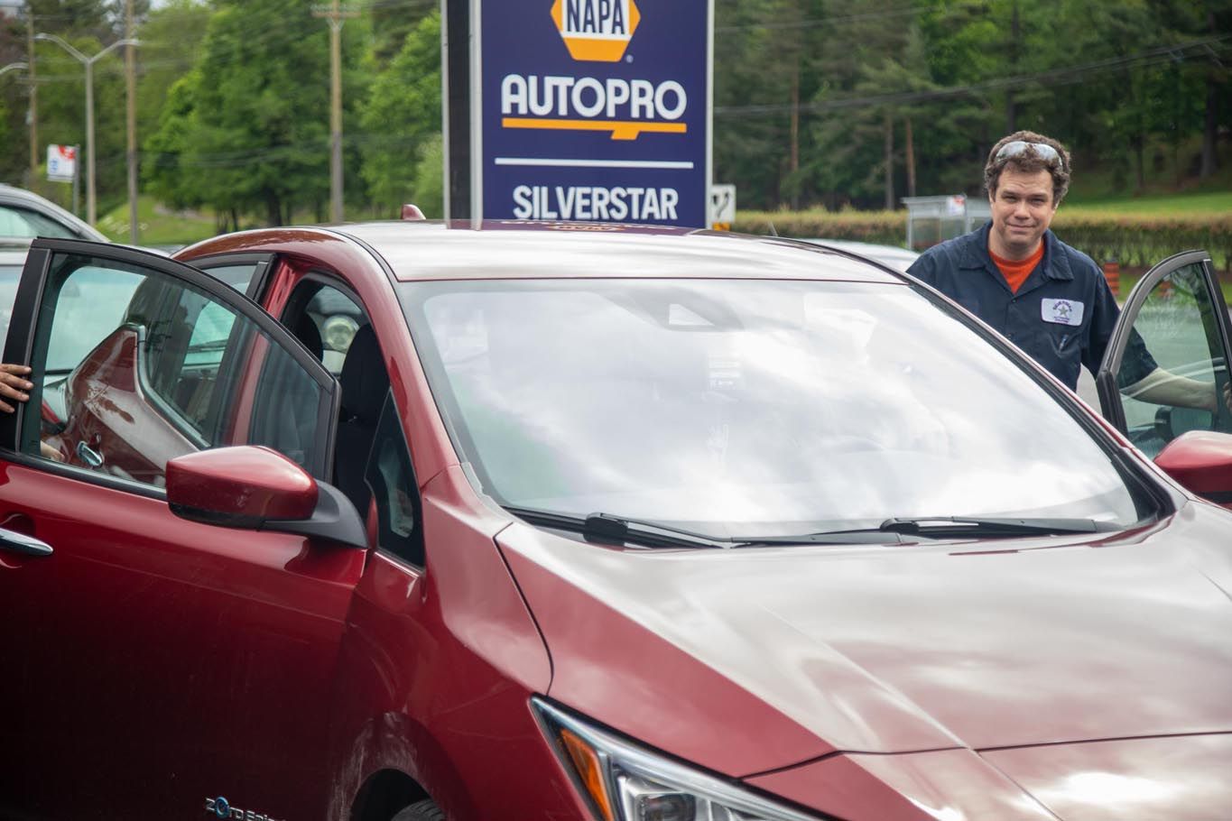 Man in black jacket standing by a red car at an AutoPro Silverstar dealership