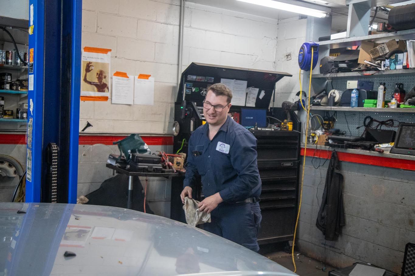 Mechanic in blue coveralls working in a garage beside a car lift and open hood