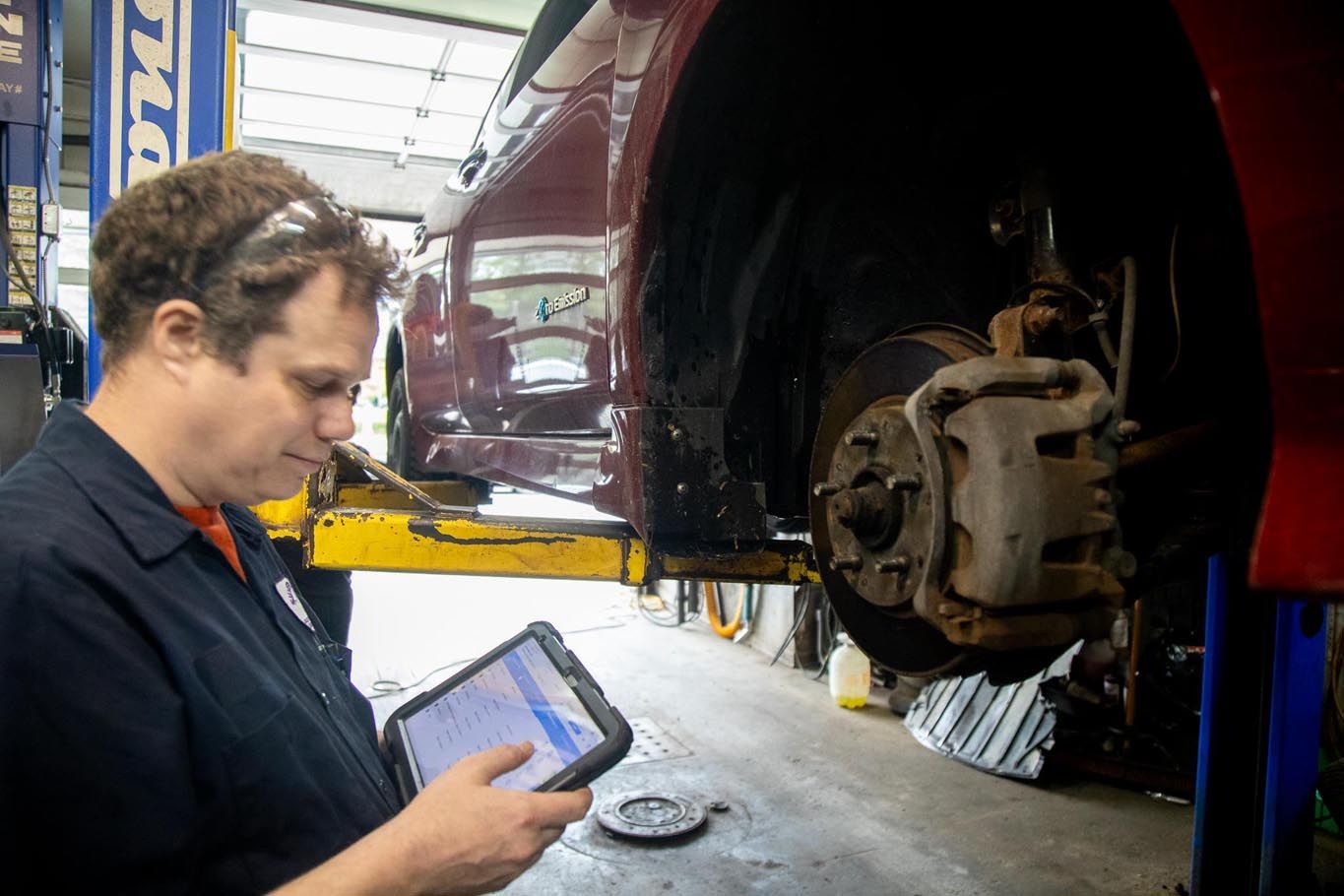 Mechanic using a tablet beside a car on a lift, with the front wheel removed in a garage