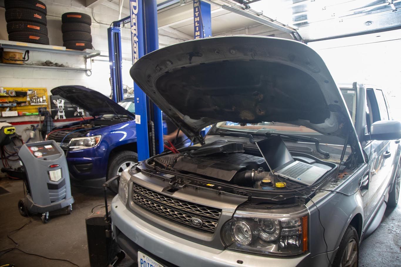 Two cars in an auto shop, with the front SUV hood open on a lift.