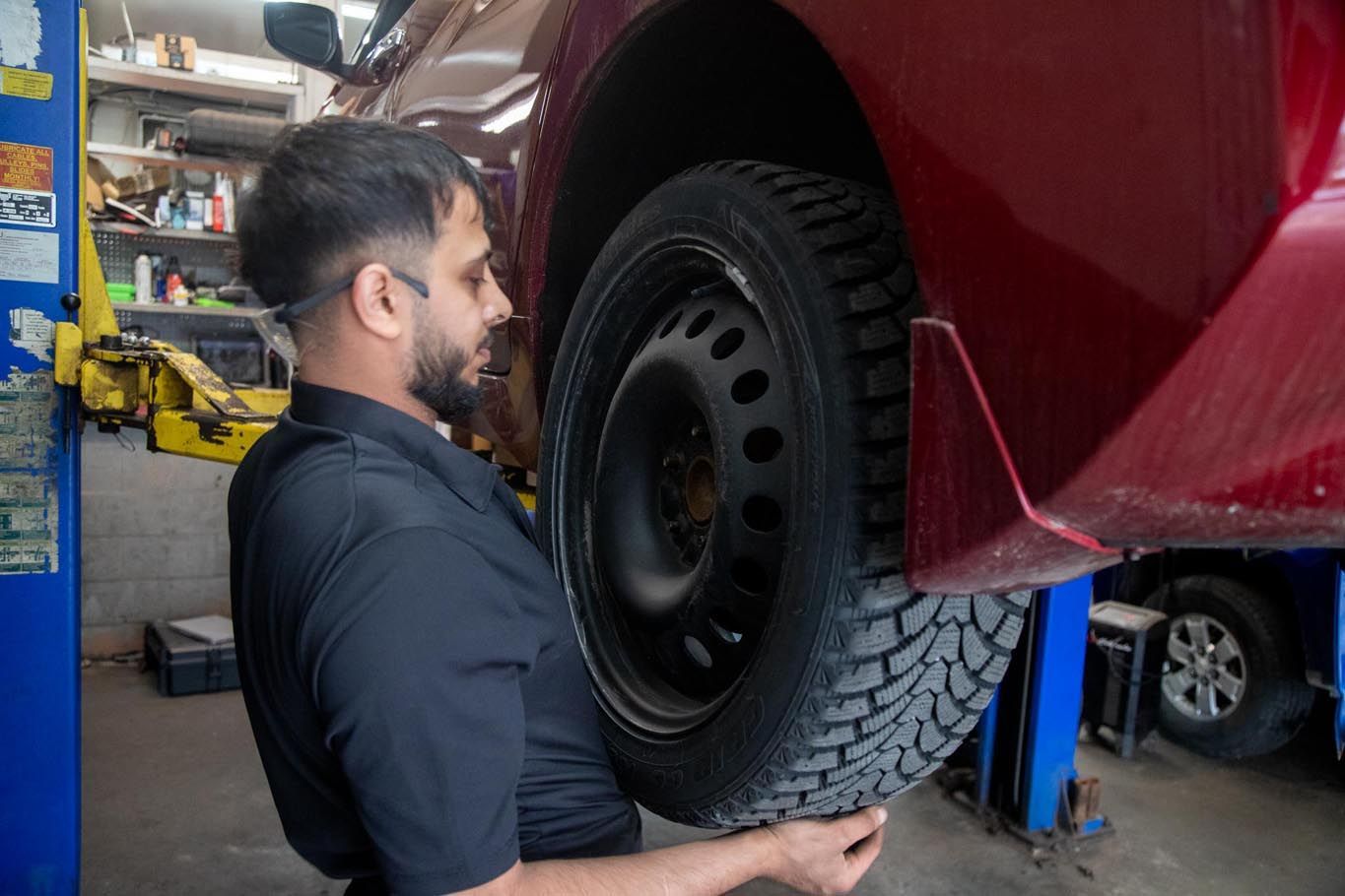 Mechanic in blue coveralls inspecting a car tire and wheel in a garage