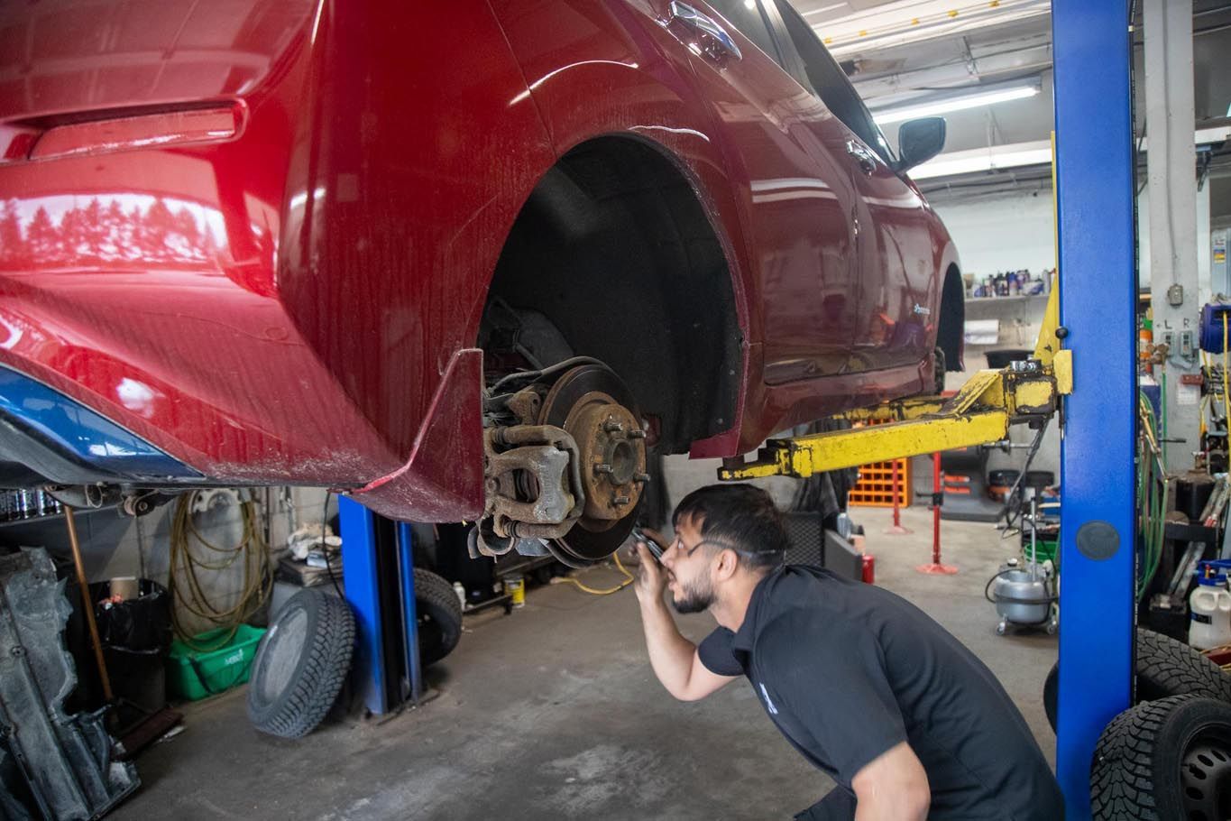 Mechanic inspecting the front wheel of a red car lifted on a hydraulic jack in a workshop