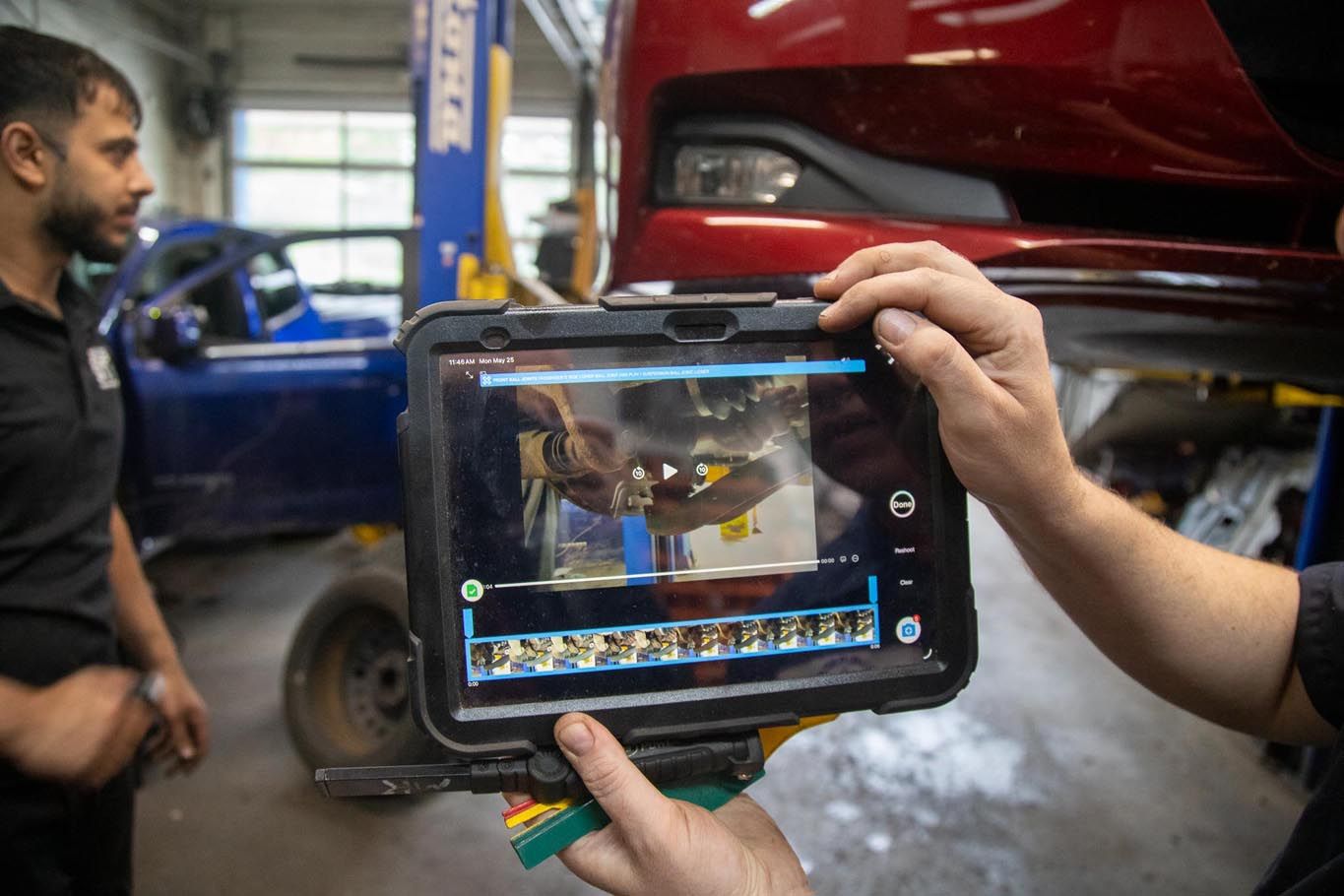 Mechanic using a tablet to inspect a car in a garage, with another person nearby