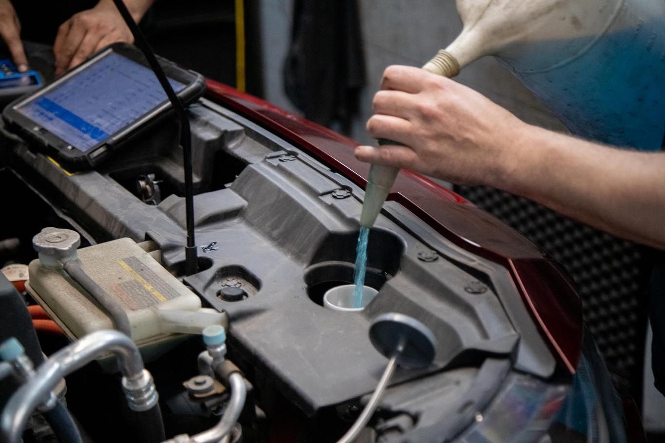 Mechanic pouring blue fluid into a car’s engine reservoir with the hood open