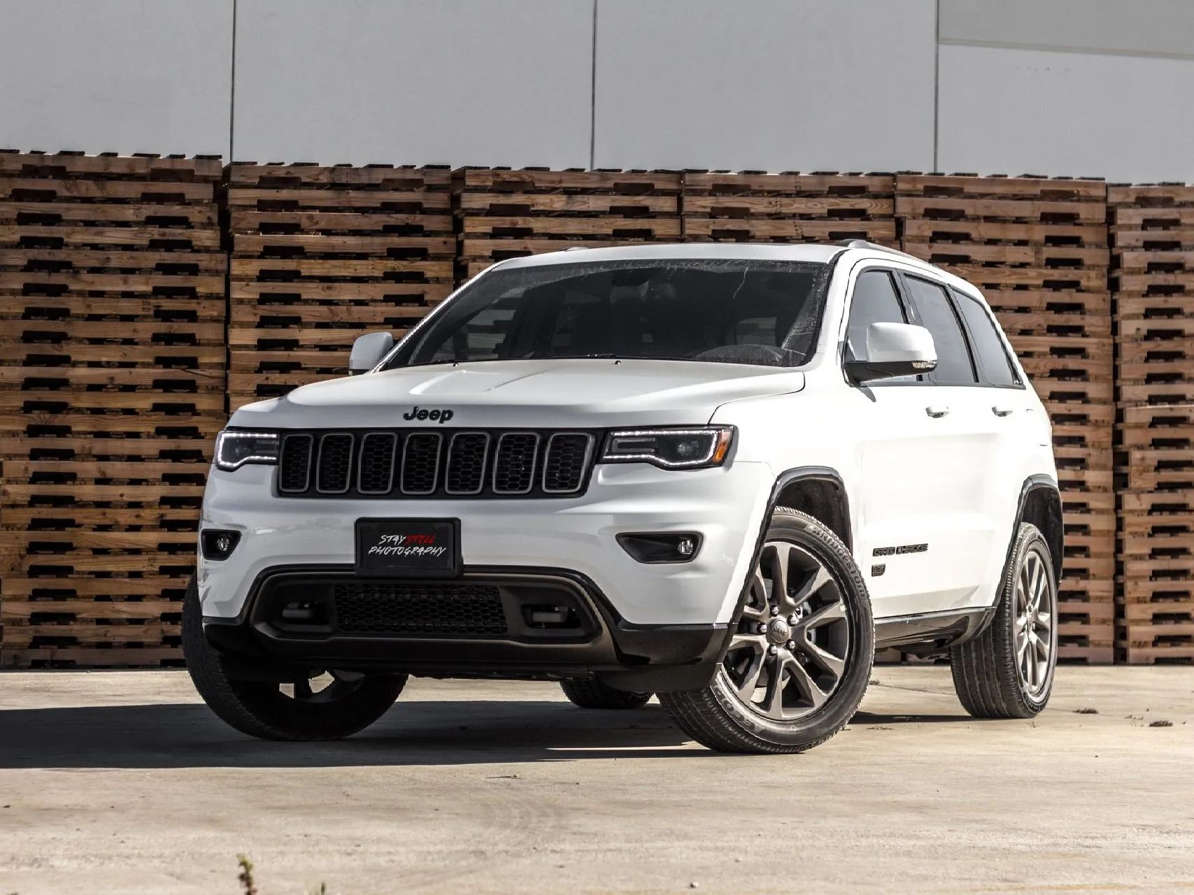 White SUV parked in front of stacked wooden pallets on a concrete lot