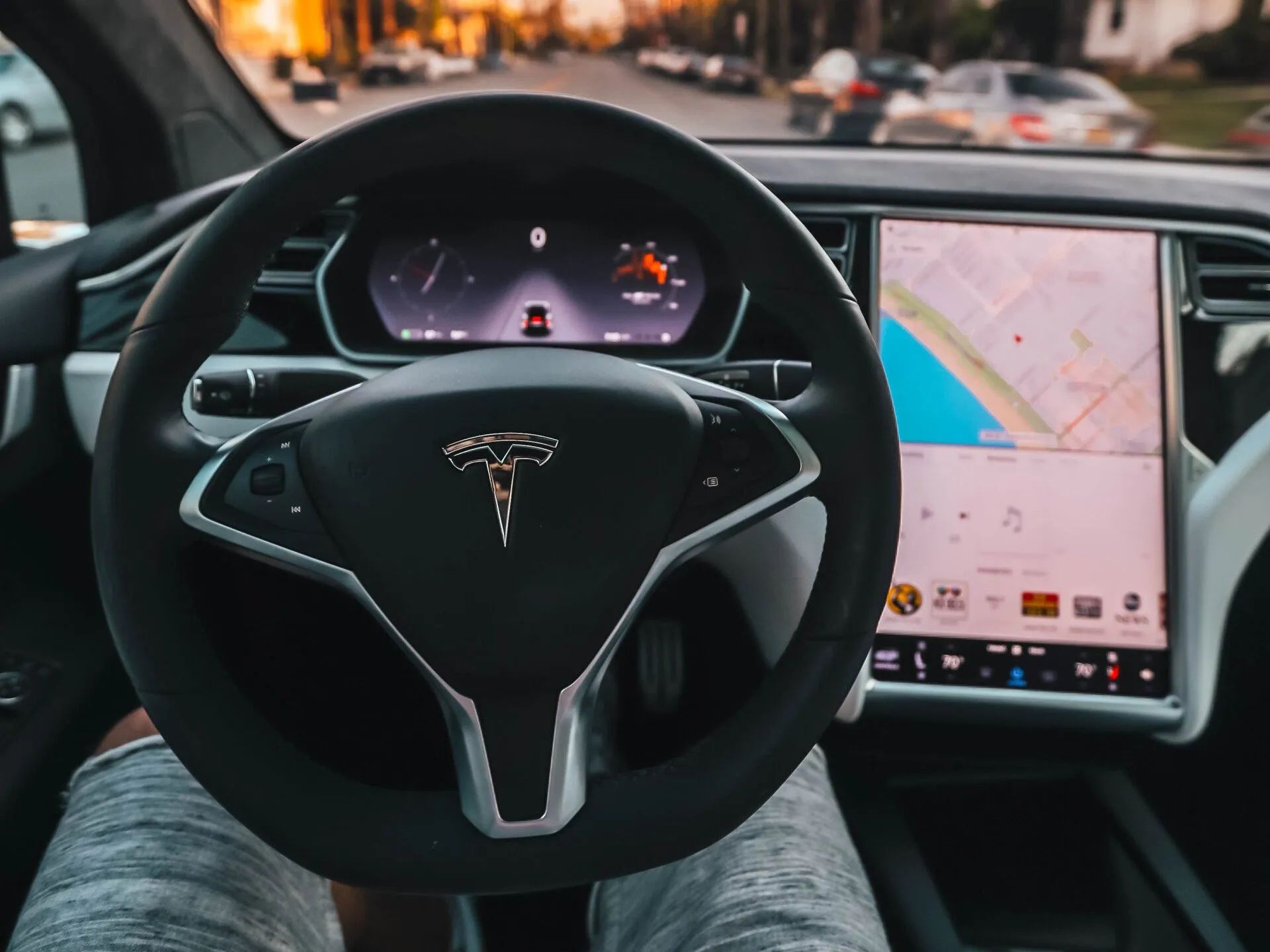 Tesla steering wheel and dashboard with center touchscreen showing a navigation map, viewed from the driver’s seat.