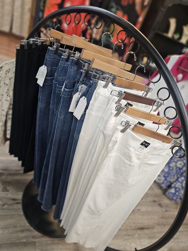 A clothing rack displaying jeans in black, denim, and white; in a store setting.