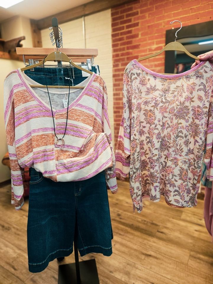 Clothing display in a boutique: striped top and denim shorts on a mannequin, floral top on a hanger, brick wall background.