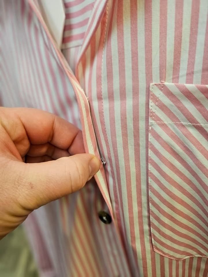 Hand holding a pink and white striped pajama shirt, showing the button closure.