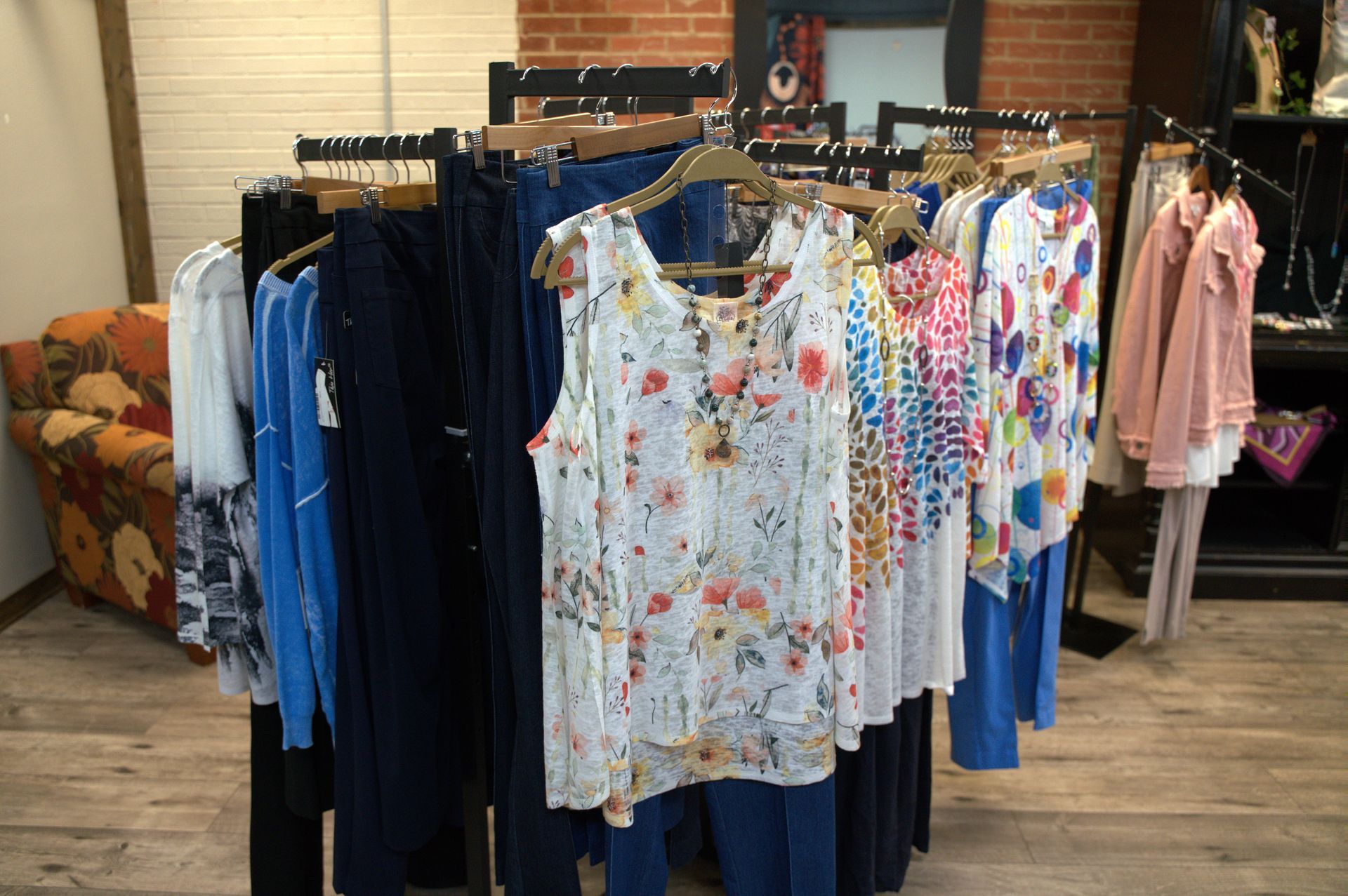 Clothes rack with a variety of women's clothing in a boutique. Includes tops, pants, and a floral-print blouse.