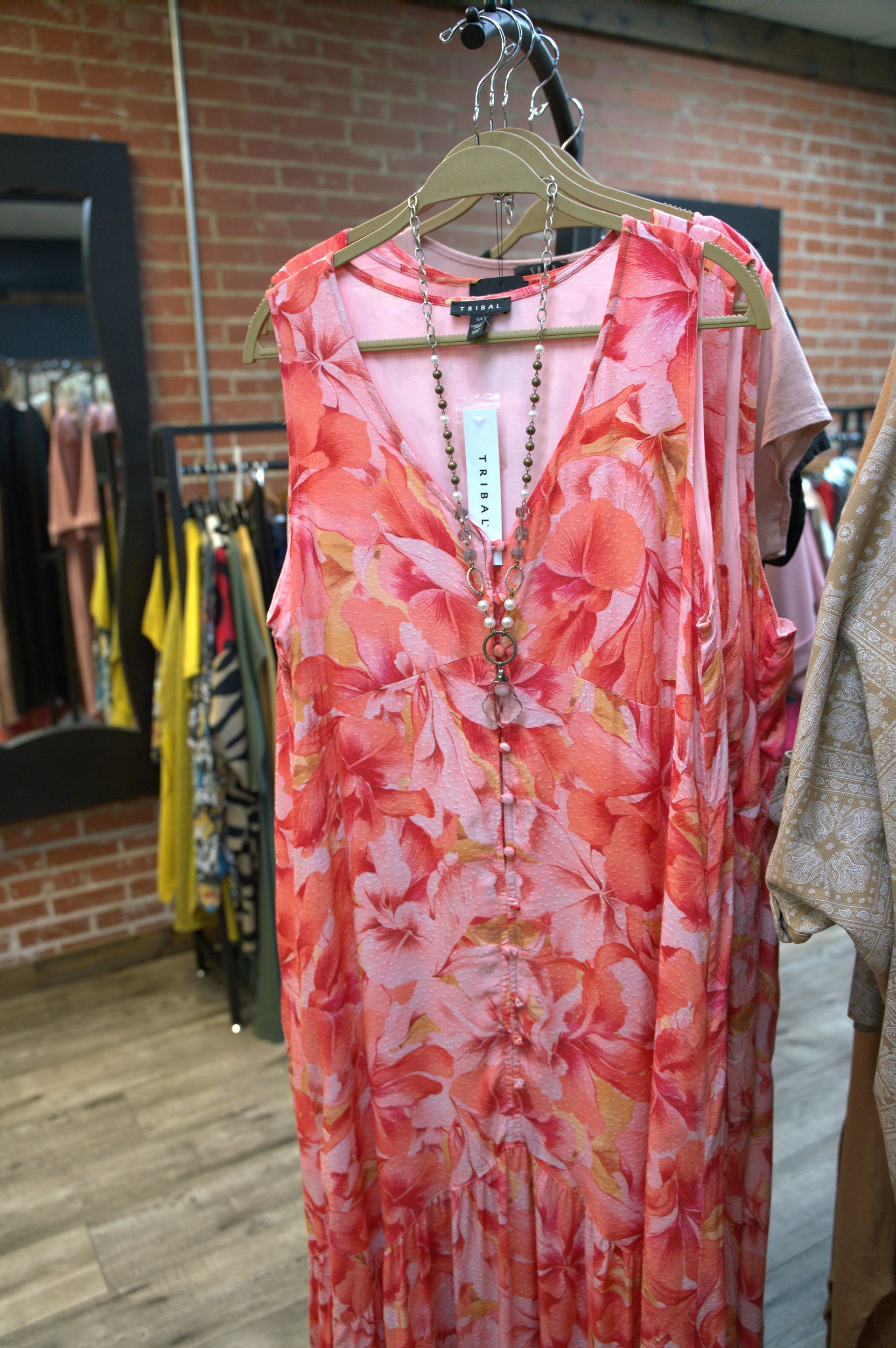 Pink and orange floral maxi dress hanging in a clothing store. A beaded necklace hangs on the dress.