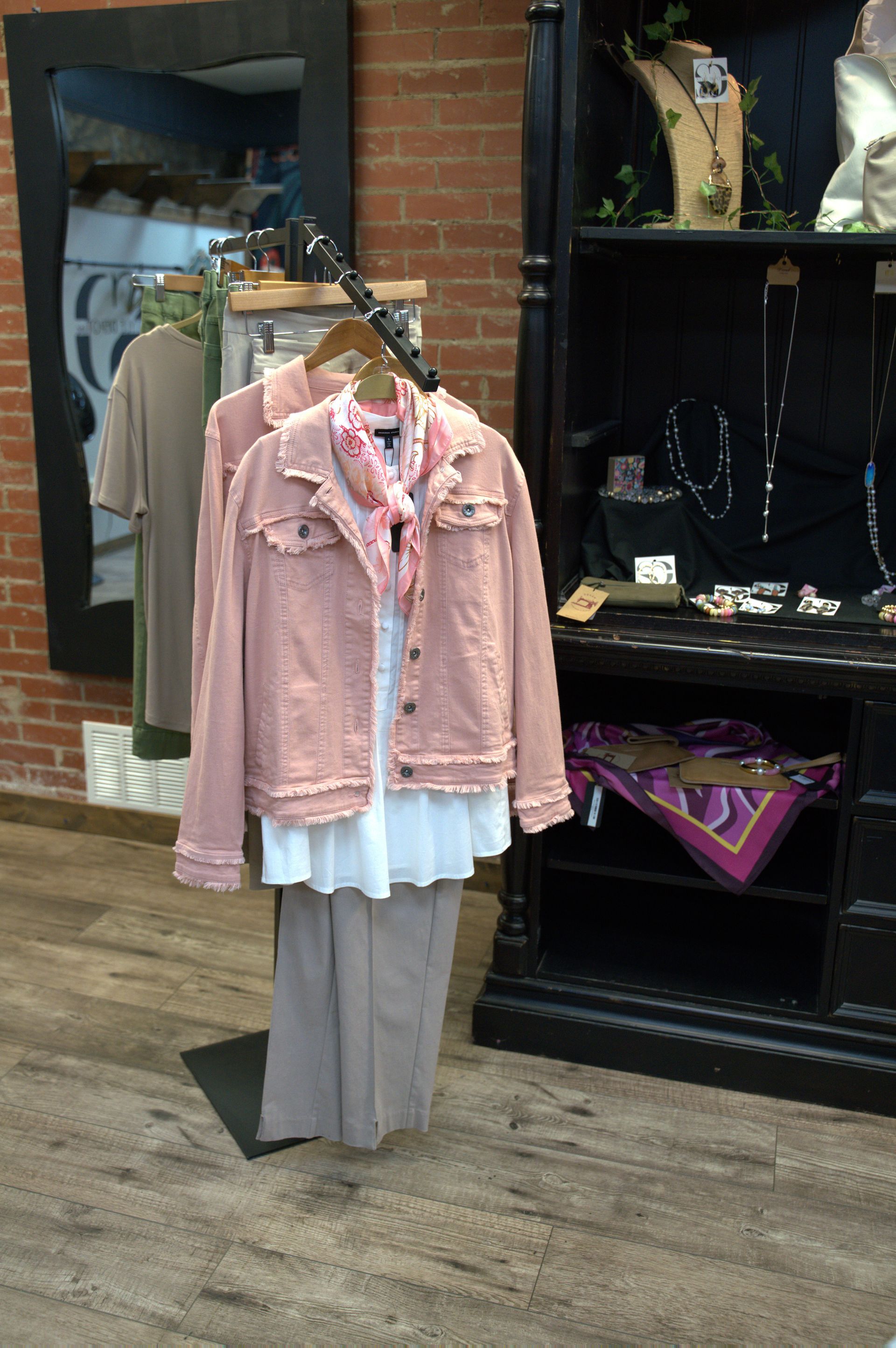 Pink jacket and blouse outfit displayed on a rack in a clothing store, with jewelry and decor in the background.