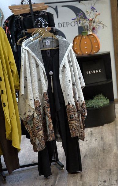 A clothing display in a boutique with a patterned jacket, black jumpsuit, and a pumpkin decoration.