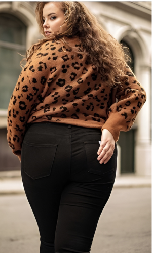 Woman in black jeans and brown leopard print sweater, looking over shoulder, hand in pocket.