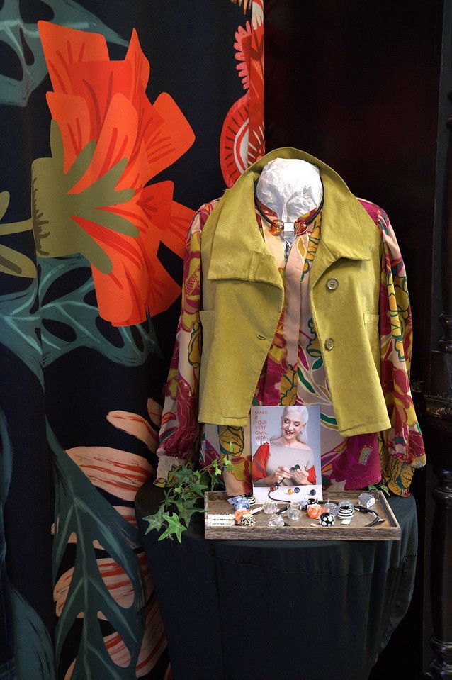 Mannequin in a shop window, wearing a floral blouse and chartreuse jacket.