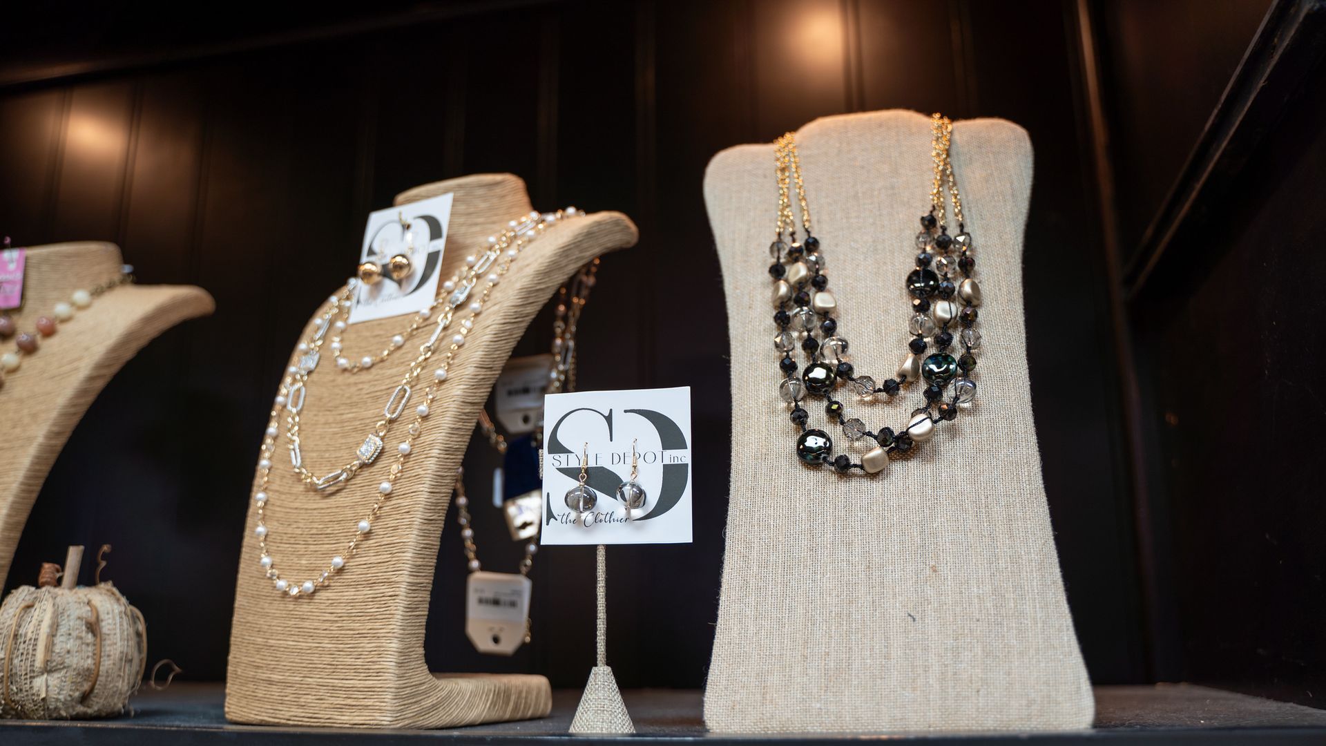 Jewelry display with necklaces and earrings on tan busts, set against a dark backdrop.