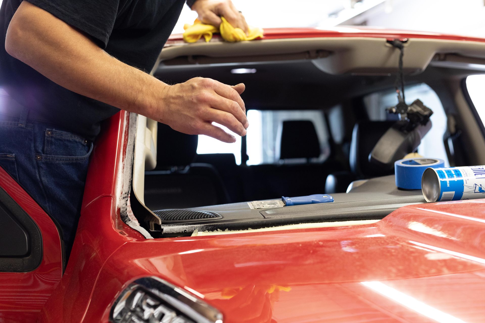 Person cleaning the windshield of a red car in a garage