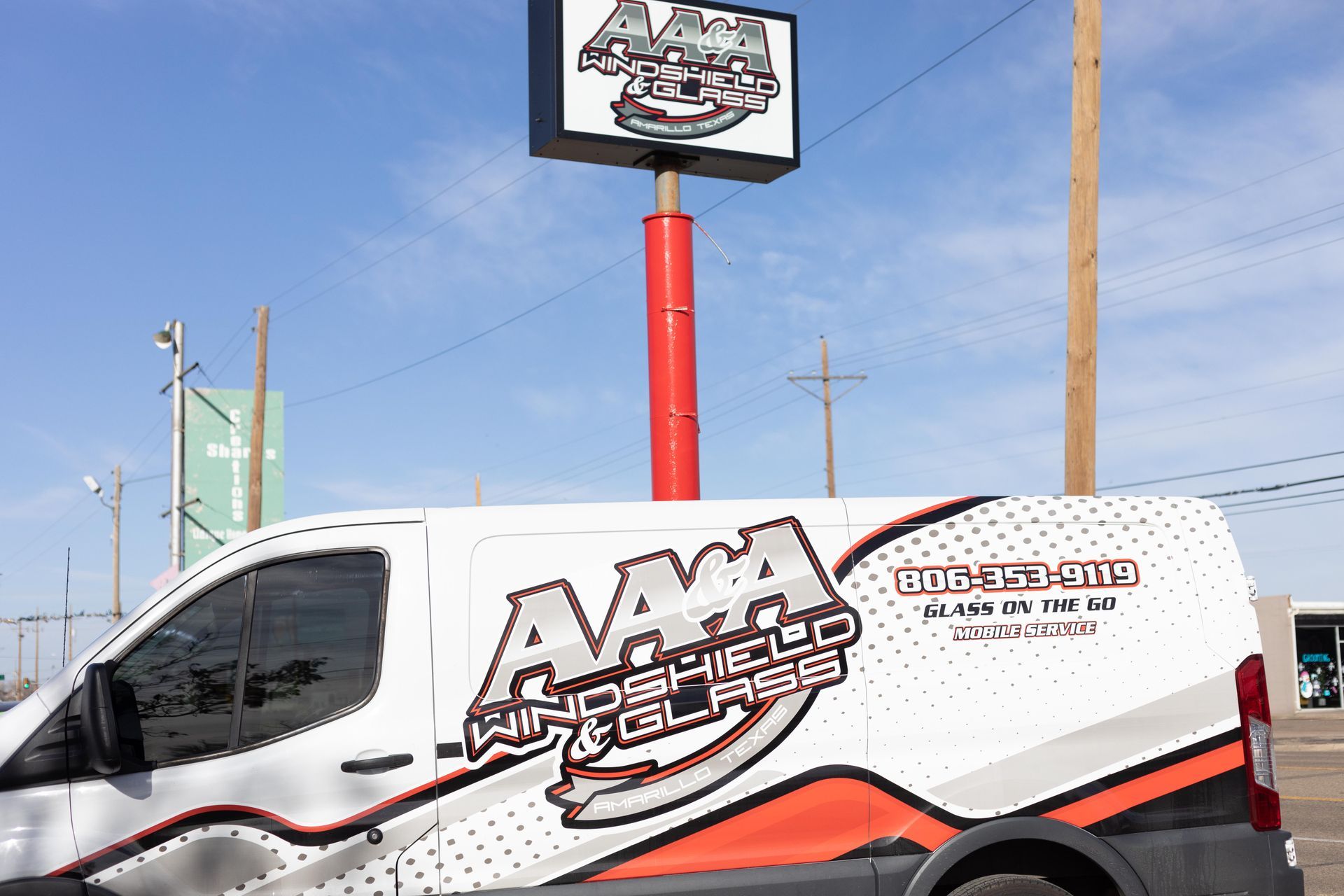 White AAA service van parked outside a roadside sign on a sunny day.