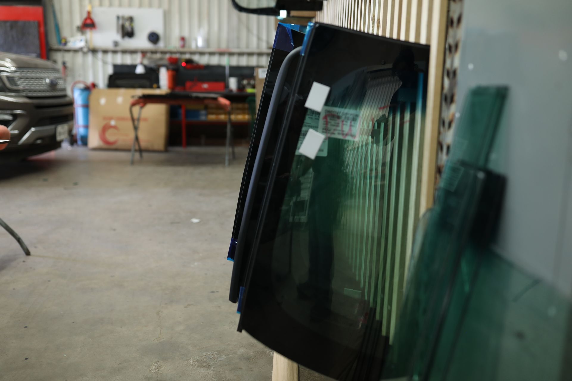 Stacked glass panels leaning in an industrial workshop with tools and equipment in the background