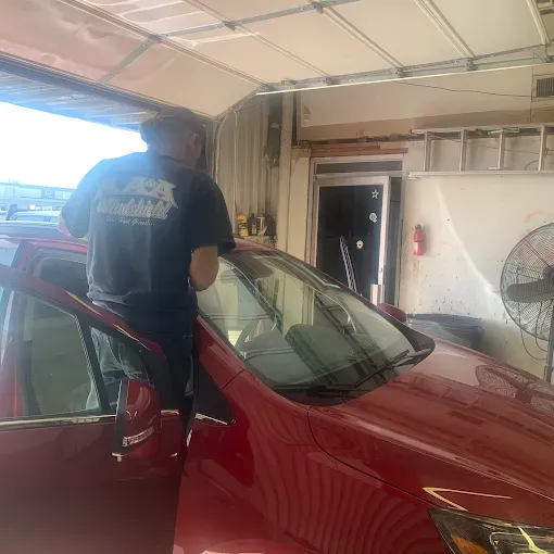 Person polishing a red car inside a garage with the door open