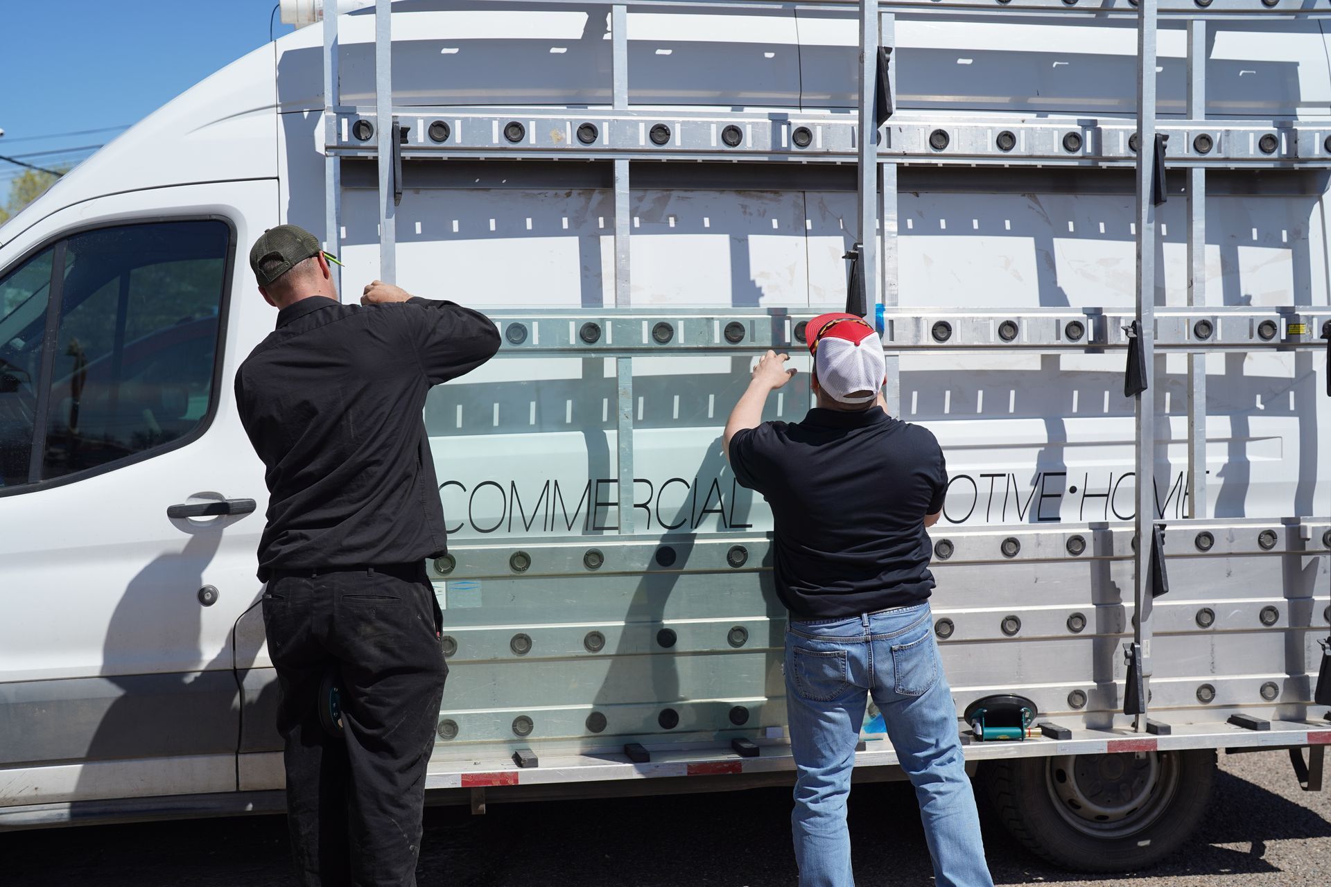 Two workers securing a glass panel to a white utility van